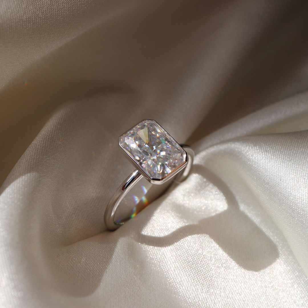 2 CT Emerald Cut Lab Grown Engagement Ring in 18K Gold. A vintage-inspired, uniquely bezel-set promise of minimalist wedding bliss.